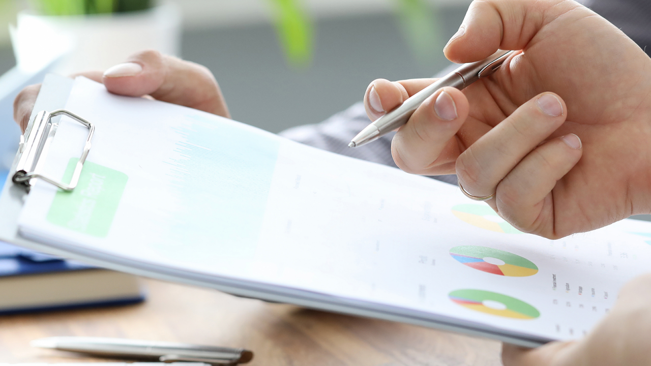 Businessmen with pen and clipboard reviewing quality analytics tools.