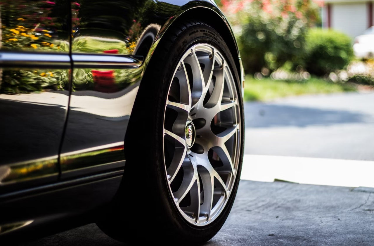 Closeup of a tire on a shiny black car parked in a driveway in a neighborhood.