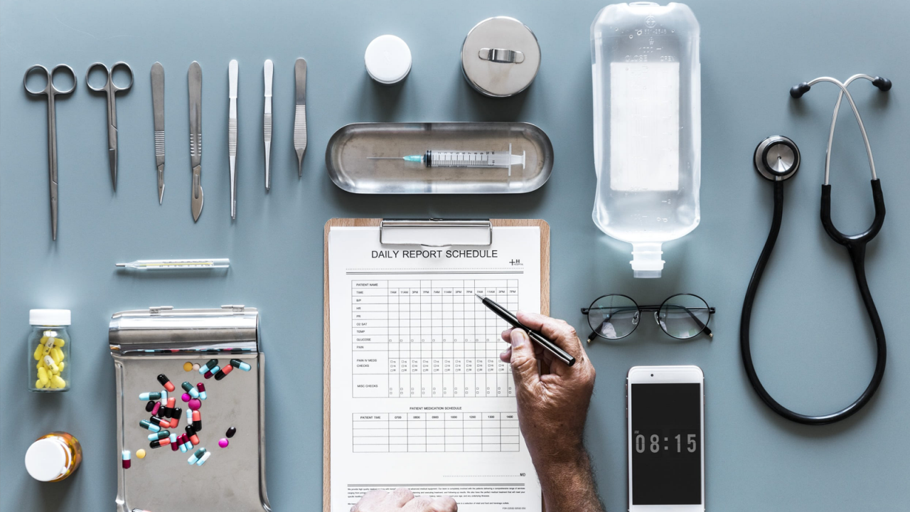 A table filled with various organized medical devices and equipment with a doctor's hand filling out a medical report.