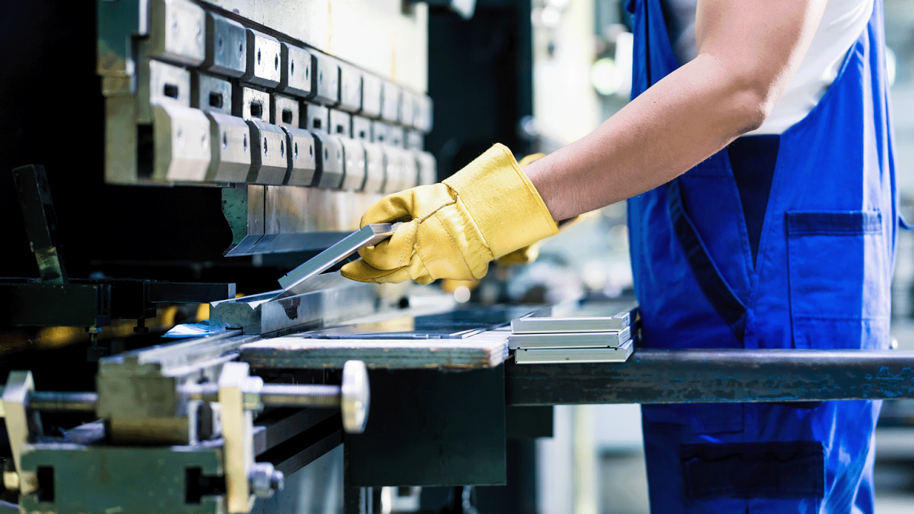 Industrial worker inspecting work piece using large manufacturing machinery while standing on the factory floor.