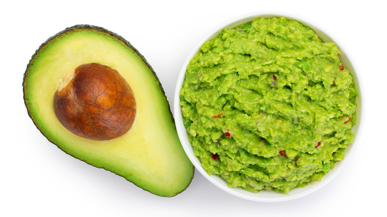 Bol de guacamole frais à côté d’un demi-avocat avec le noyau.