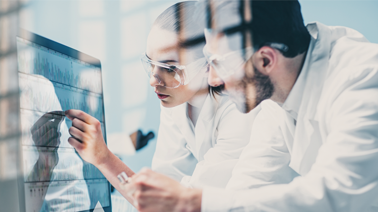 白衣とゴーグルを着用した2人の製薬科学者がコンピュータで統計的プロセス管理をしています。